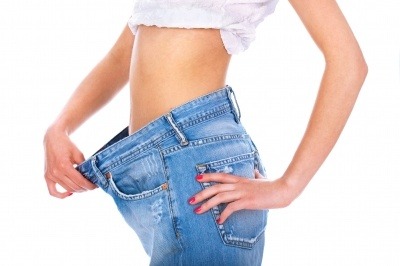 Woman showing how much weight she has lost from her stomach, wearing blue jeans.