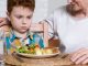 Close-up of a little boy looking malevolently at a dinner plate full of healthy food with his mother looking kindly on.