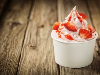 Ripe red tropical strawberries and vanilla ice frozen yogurt cream for a healthy refreshing cold summer dessert in a takeaway tub on an old rustic wooden table with copyspace