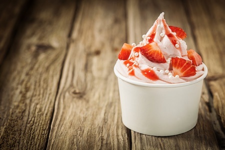 Ripe red tropical strawberries and vanilla ice frozen yogurt cream for a healthy refreshing cold summer dessert in a takeaway tub on an old rustic wooden table with copyspace