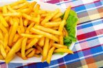 French fries with lettuce on a white plate, on a plaid tablecloth.. One of the foods associated with acrylamide formation.