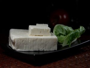 Slabs of feta cheese with basil leaves on a black background.