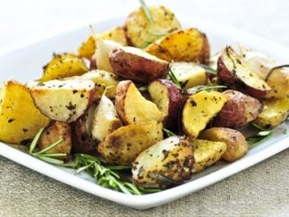 A white dish with rasted potatoes and various herbs.