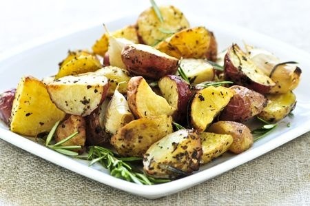 A white dish with rasted potatoes and various herbs.