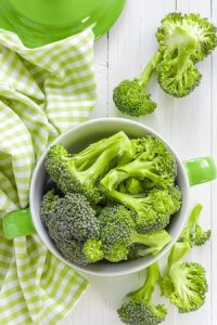 Broccoli in a white cup with green handles. Green and white check dishcloth.