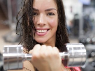 Beautiful woman doing a handbell curl. Looking sweaty.. Whey protein isolate might be one of the ingredients she takes for a her gym work.