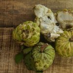 Top view closeup nice broken ripe sugar apples with brown seed near unbroken sweet-sops on wooden table background