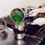 Chef pouring spinach through a sieve after blanching.
