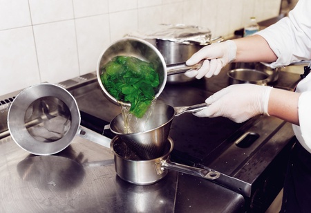 Chef pouring spinach through a sieve after blanching.