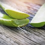 Cut halves of aloe leaves on a wooden table.