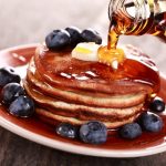 Pouring maple syrup on stack of pancakes.