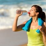 Fitness beautiful woman drinking water and sweating after exercising on summer hot day in beach female athlete after work out. An example of sports nutrition.