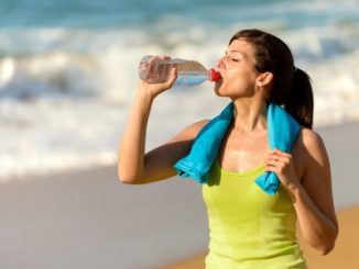 Fitness beautiful woman drinking water and sweating after exercising on summer hot day in beach female athlete after work out. An example of sports nutrition.