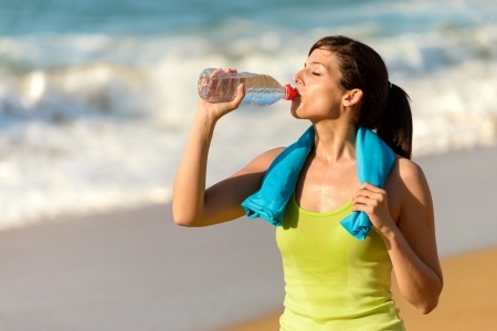 Fitness beautiful woman drinking water and sweating after exercising on summer hot day in beach female athlete after work out. An example of sports nutrition.