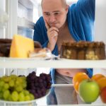Corpulent man contemplating unhealthy food rather than healthy food. Could he be thinking if there are any trans fats in these products ?