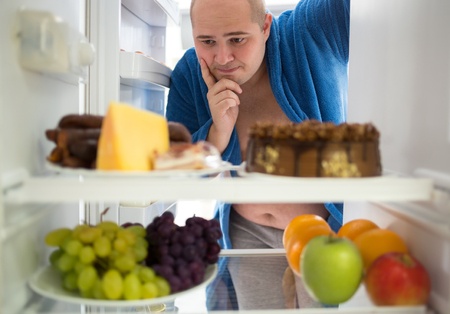 Corpulent man contemplating unhealthy food rather than healthy food. Could he be thinking if there are any trans fats in these products ?