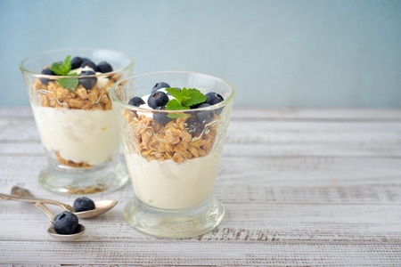 Granola with yogurt and blueberry in glass on wooden background.