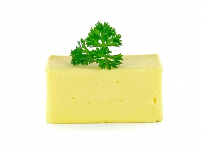 A bar of butter with a parsley leaf on top, on a white background.