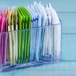 Packets of artificial sweeteners in glass container sitting on bright blue wooden table