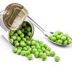 Opened tin with green peas on spoon. Isolated on white background