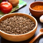 raw textured vegetable or soy protein, called also soy meat in wooden bowl with raw vegetables on kitchen towel and paprika powder in the back. photographed on dark wood with natural light (selective focus, focus one third into the soy meat)