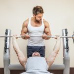 21828129 - a handsome young muscular sports man doing weight lifting and gets help from his friend.