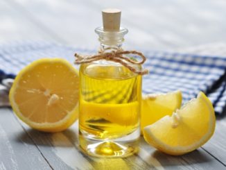 Lemon oil in a glass bottle with fresh lemon on wooden background