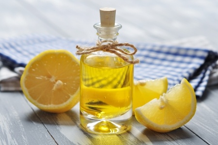 Lemon oil in a glass bottle with fresh lemon on wooden background