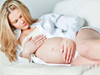 Pregnant woman lying on her side, clutching at her pregnant stomach or feeling her bump.