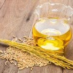 Rice bran oil in bottle glass and unmilled rice on wooden background