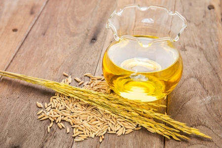 Rice bran oil in bottle glass and unmilled rice on wooden background