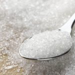 Close-up of granulated sugar in spoon and sugar pile.