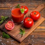 Glass of fresh tomato juice and tomatoes on a wooden cutting board