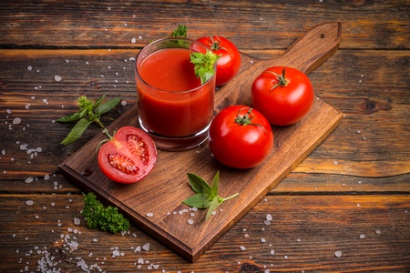 Glass of fresh tomato juice and tomatoes on a wooden cutting board