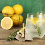 Tasty cool beverage with lemon and thyme, on wooden background