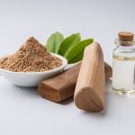 Chandan or sandalwood powder with traditional mortar, sandalwood sticks, perfume or oil and green leaves. selective focus
