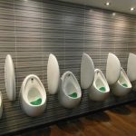 A bank of male urinals in a well lit room.