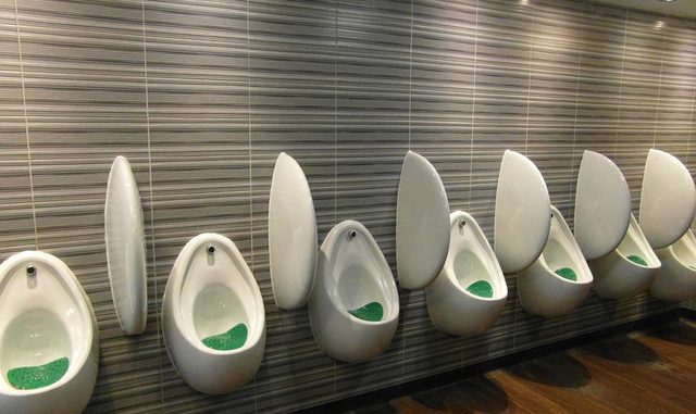 A bank of male urinals in a well lit room.