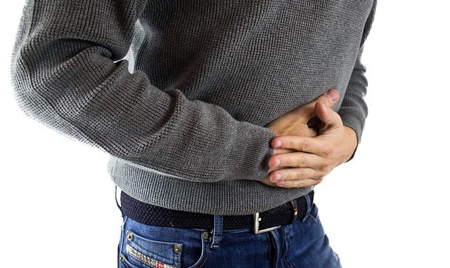 Man in grey jumper clutching stomach or abdomen. Photo shows mid -part of body, no head. Could he be suffering with IBS, diarrhea/diarrhoea or constipation.