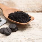 Activated carbon in a wooden spoon with tablets on a fawn wooden background.