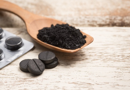 Activated carbon in a wooden spoon with tablets on a fawn wooden background.