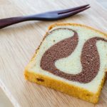 Slice of marbled butter cake with a stylish brown fork on a wooden table slab.