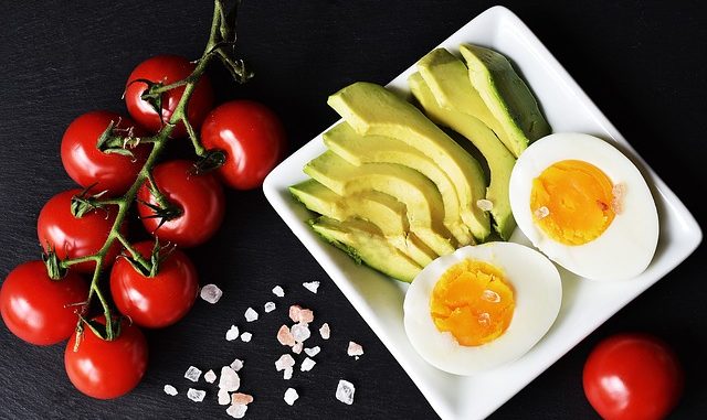 Tomatoes, avocado, egg on a white dish with black background. Foods for a keto diet.