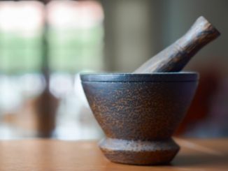 Pestle and mortar on a brown wooden table in a kitchen.