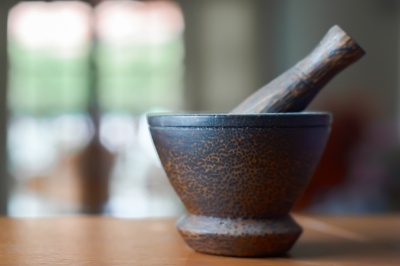 Pestle and mortar on a brown wooden table in a kitchen.
