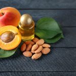 Bottle of apricot oil with fresh fruit and kernels on wooden table