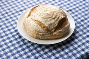 A sourdough loaf on a white plate, laid on a blue and white check tablecloth.
