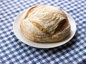 A sourdough loaf on a white plate, laid on a blue and white check tablecloth.