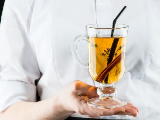 The unidentified waiter holding a glass with hot Amaro cocktail with apple juice and cinnamon