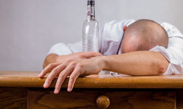 Man asleep on table with empty bottle in his grasp.